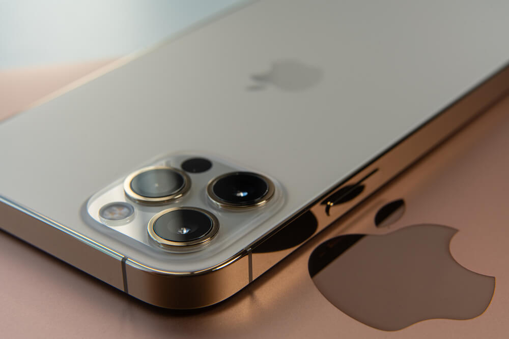 Iphone 12 leżący na Macu. Obydwa sprzęty w szarych, metalicznych kolorach.