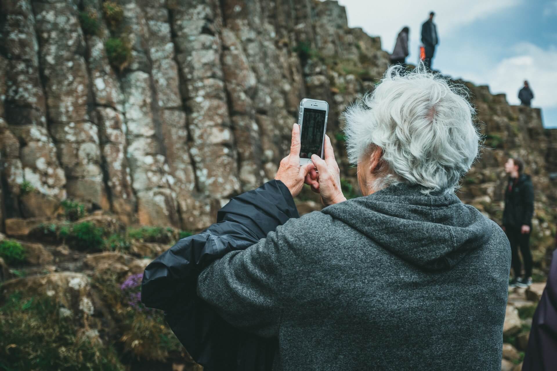 Starszy człowiek robiący zdjęcie smartfonem krajobrazu, gór. 