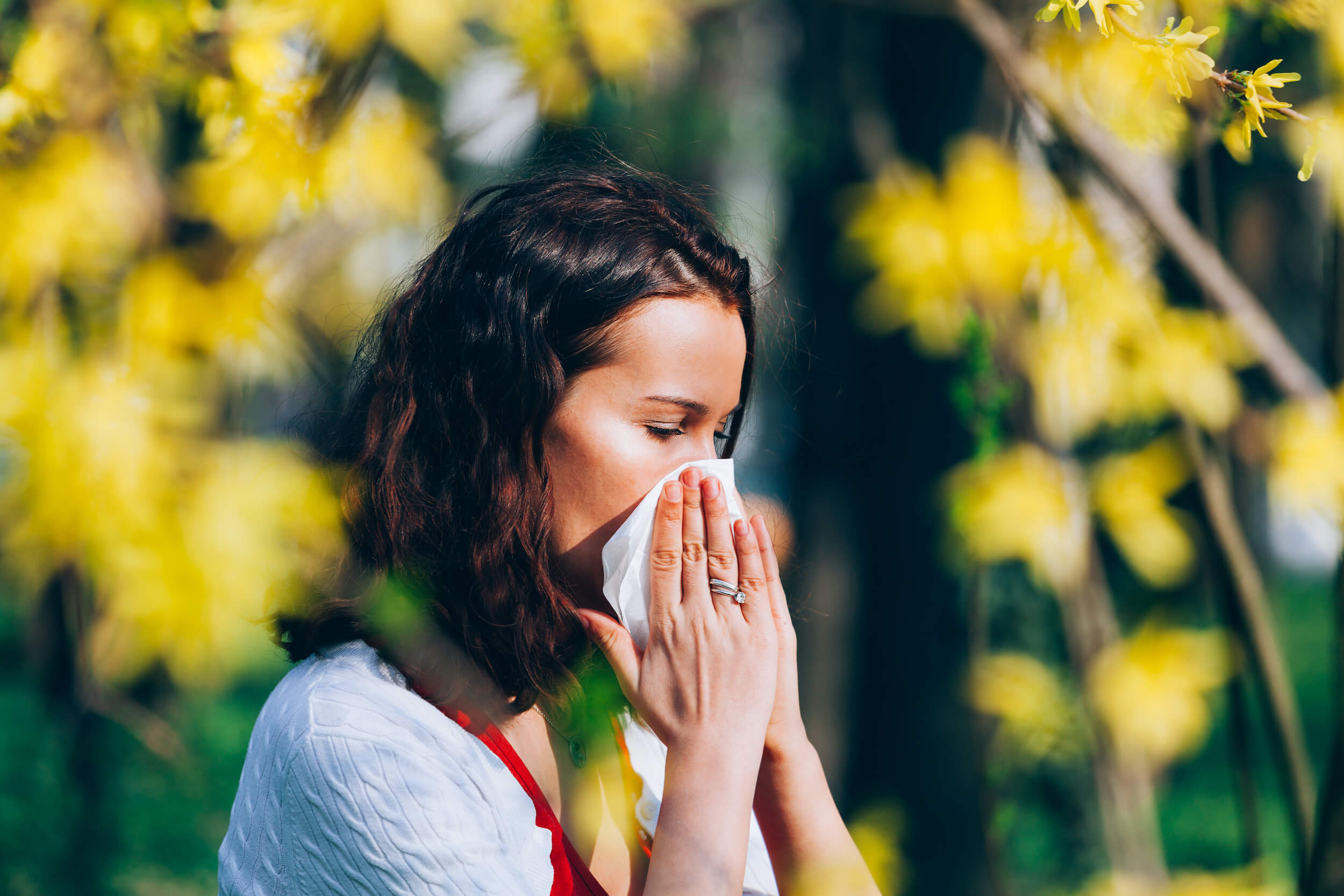 kobieta zmagająca się z alergią w otoczeniu żółtych krzewów