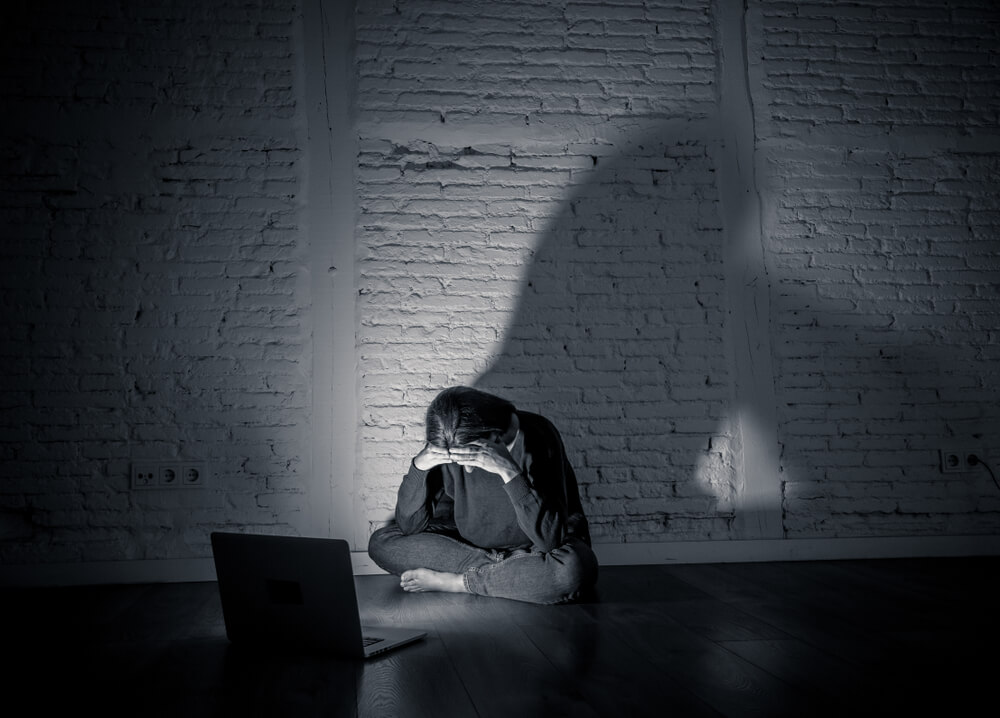 Dziewczyna płacząca przed laptoem. na ścianie jej cień. Kolorystyka zdjęcie w odcieniach szarości. 
