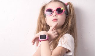 Dziewczynka w okularach przeciwsłonecznych, z różowym smartwatchem na dłoni.